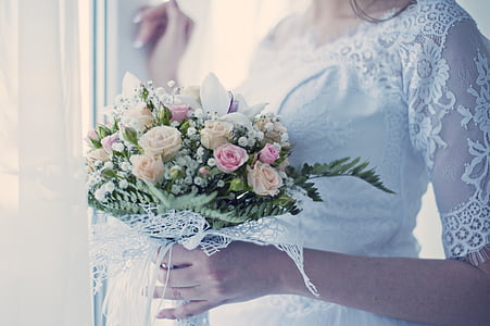 woman in white floral gown holding bouquet of flowers beside window thumbnail