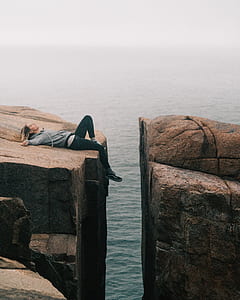 woman lying on brown rocky mountain near water during daytime thumbnail