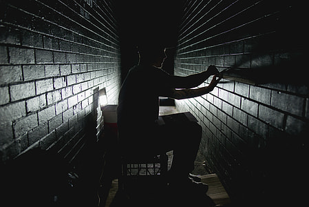 man, on chair, brick wall, dim-lit thumbnail