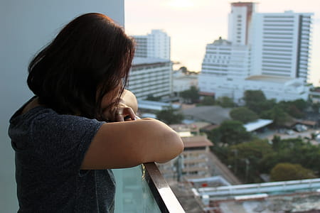 Urban Lifestyle An Asian lady looks out at high-rise city buildings from a balcony thumbnail
