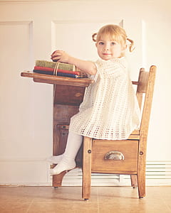 girl in white knitted dress sitting on brown wooden school chair thumbnail