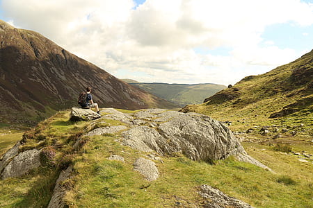 man sitting on stone near mountain under white cloudy sky during daytime thumbnail