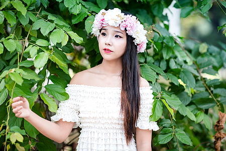 woman wearing flower headdress and off-shoulder dress standing next to leafy plant thumbnail