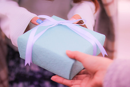person passing square teal gift box with white bow to another person with blue manicure thumbnail