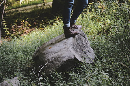 person wearing boots standing on rock surrounded with green grass thumbnail