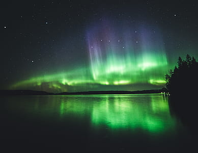 Aurora lights over calm body of water during night time with starry sky thumbnail