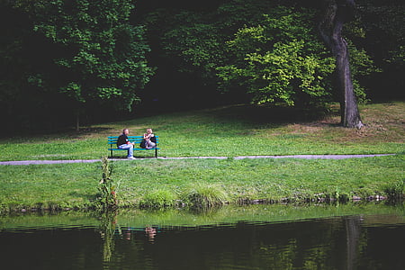 two person sitting on bench near body of water thumbnail