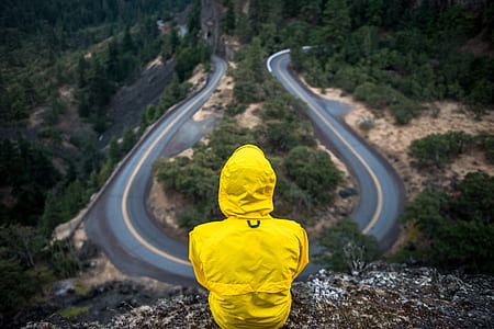 person wearing yellow coat sitting on mountain edge thumbnail