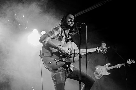 grayscale photo of man playing guitar while singing thumbnail