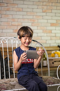 boy holding tablet computer while sitting on bench thumbnail