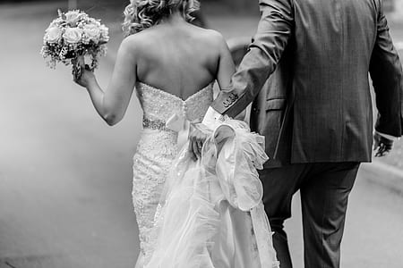 grayscale photo of groom beside bride holding blower bouquet facing back thumbnail