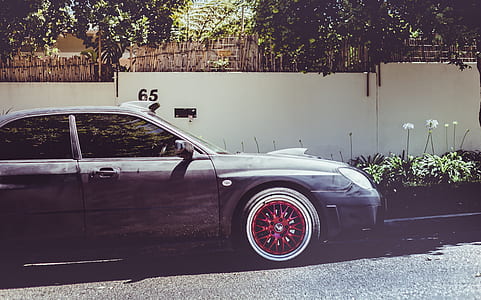 black sedan parking on road near white wall thumbnail