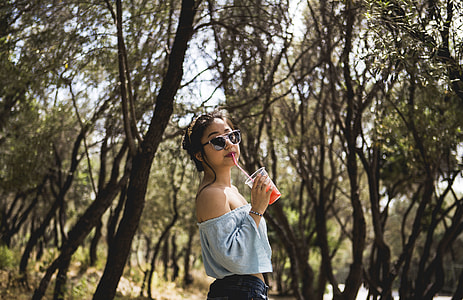woman holding plastic cup sipping under trees thumbnail
