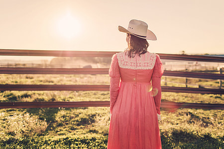 photography of woman in pink dress and white hat facing green grass field thumbnail