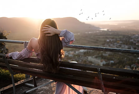 woman lying on a black wooden bench during sunset with flock of birds on the horizon thumbnail