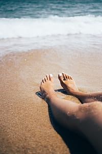 Sandy feet on the beach with waves in the background thumbnail