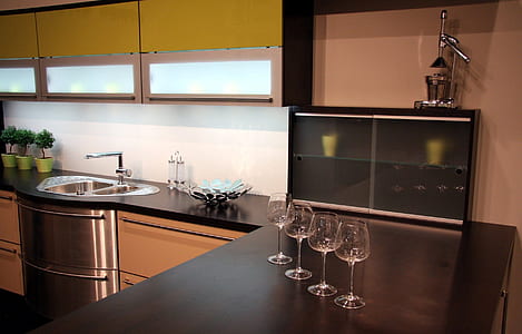 four clear wine glasses on brown wooden kitchen desk near black wooden cabinet thumbnail