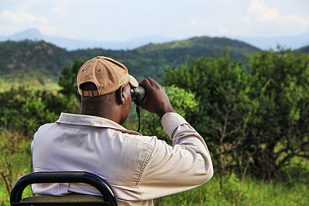 man using binoculars facing trees and mountains thumbnail