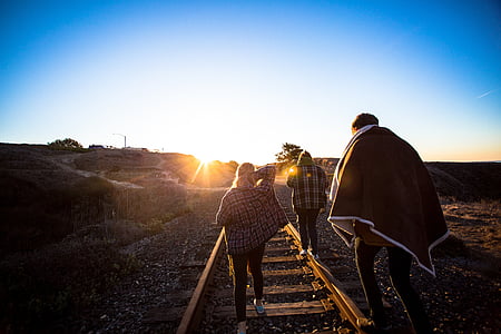 woman wearing red, white, and black dress shirt walking on railway during daytime thumbnail