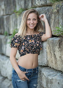woman in black and yellow floral crop top and blue jeans leaning on wall thumbnail