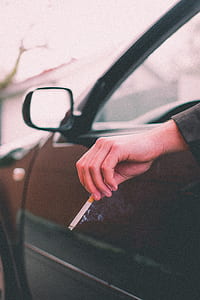 person riding car with left arm on window holding single cigarette thumbnail