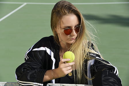 woman wearing black and white jacket while holding tennis ball near court thumbnail