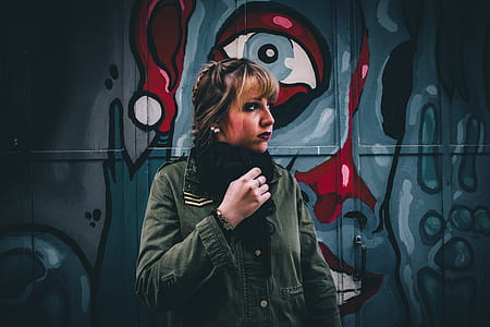 woman wearing grey jacket standing back of graffiti wall thumbnail