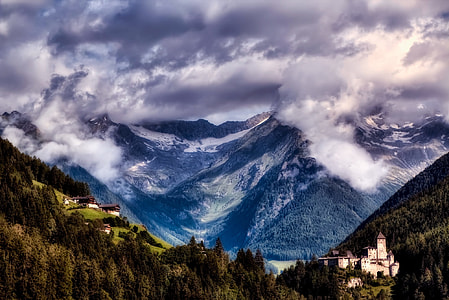 snow mountain covered with white clouds and forest below it thumbnail