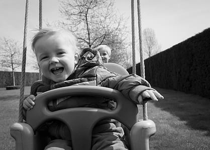 grayscale photo of boy sitting on swing chair thumbnail