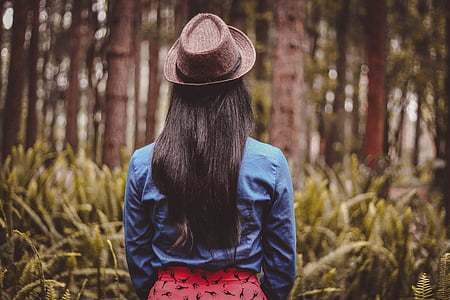 woman wearing blue jacket and red bottoms with fedora hat in woods thumbnail