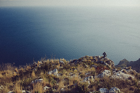 person  standing near cliff with viewing body of water during cloudy day thumbnail