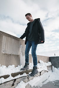 man wearing black jacket holding on brown wall thumbnail
