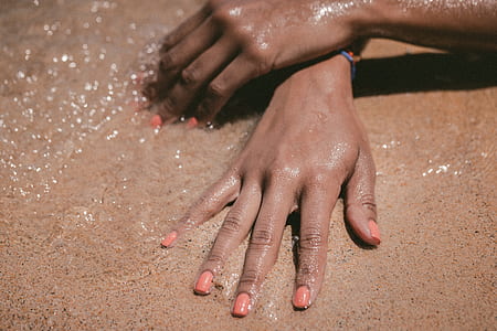 person's hands on white sand near body of water thumbnail