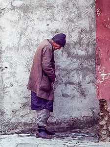 man wearing coat standing beside wall thumbnail