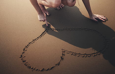 close-up photo of woman drawing heart on sand thumbnail