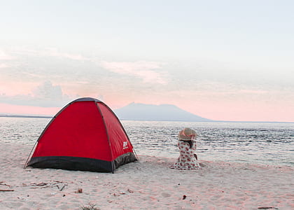 person sitting on shoreline beside red tent thumbnail