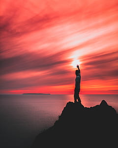 man standing on rock monolith while raising right hand thumbnail