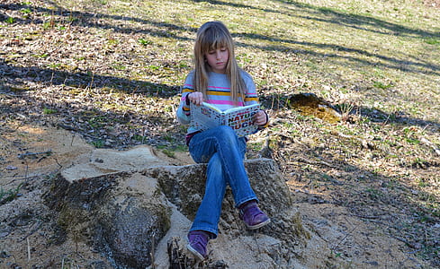 girl holding book while sitting on stone thumbnail