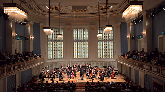 orchestra performing on stage in-front of people inside building thumbnail