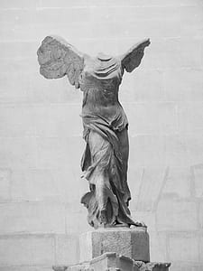 concrete angel statue with broken head beside gray concrete wall thumbnail