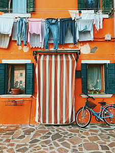 clothes hanged in front of orange building above blue bicycle parked near pathway thumbnail