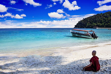 man sitting on sand near white boat and seashore during daytime thumbnail