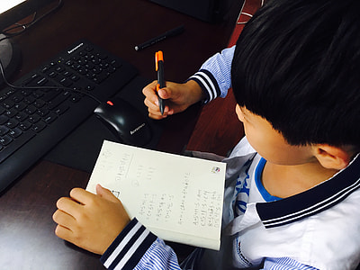 boy sitting on chair in front of monitor holding pen and book thumbnail