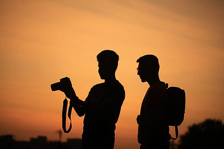 silhouette of two men carrying camera and backpack during sunset thumbnail