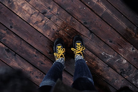 person wearing black-and-yellow sneakers on brown wooden floor thumbnail