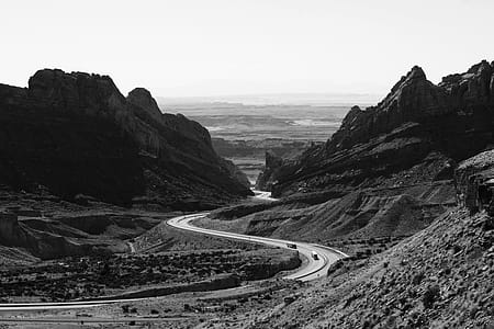 Grayscale Photo of Roadway Surrounded With Rocky Mountains thumbnail