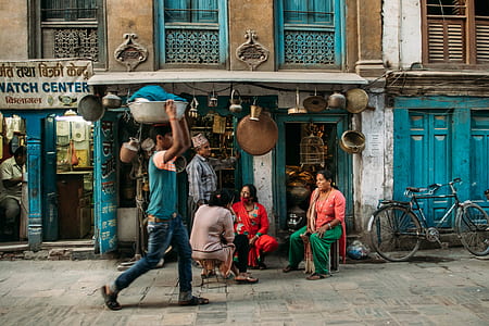person wearing blue and pink shirt carrying basin with clothes on head while walking beside four persons on concrete pathway during daytime thumbnail