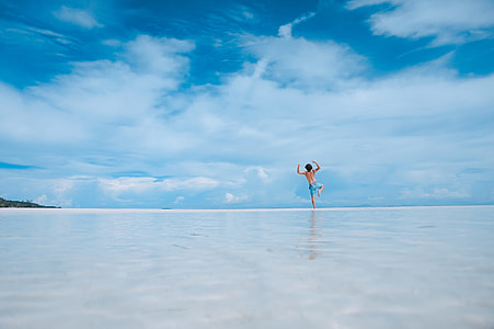 man jumping on wet sandy beach under blue cloudy skies thumbnail