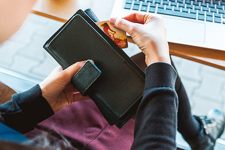 person wearing black long-sleeved shirt holding black leather long wallet pulling out MasterCard thumbnail