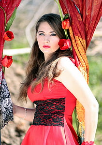 woman wearing red and black floral sleeveless dress holding curtain with flowers thumbnail